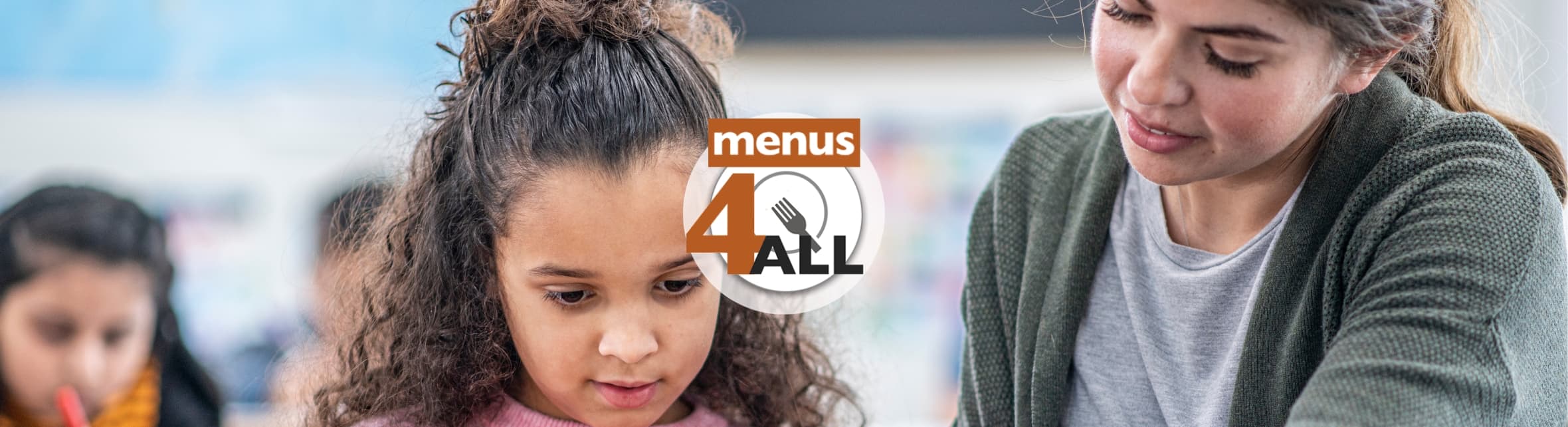 Primary grade student focusing on tablet while teacher gives directions. With Menus4ALL logo.